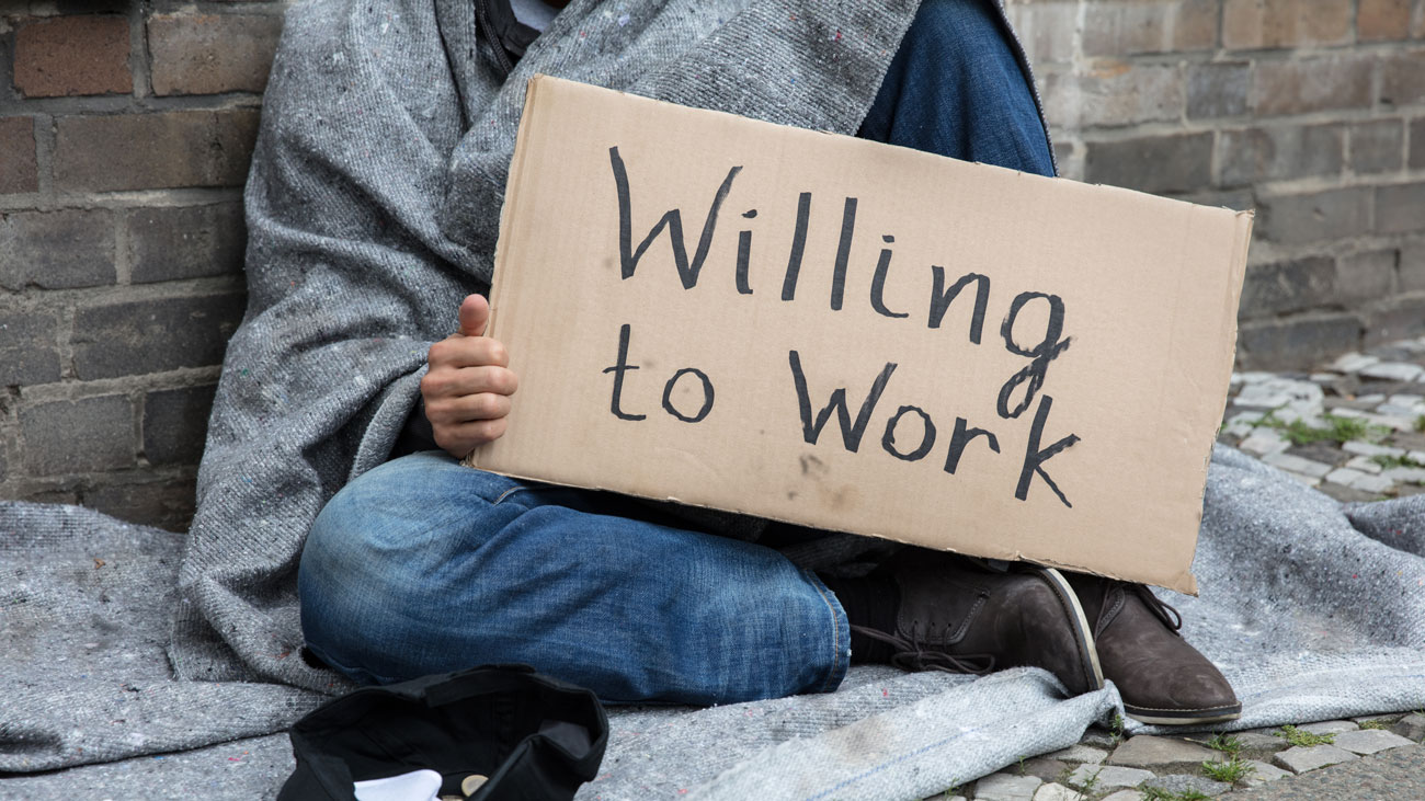 A homeless person holding 'willing to work' sign